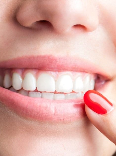 Close up of person with red fingernails touching their lower lip while smiling