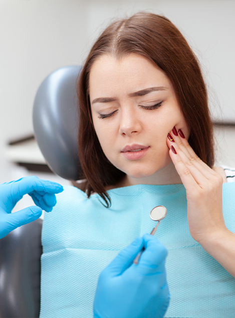 Young woman in dental chair touching her cheek in pain