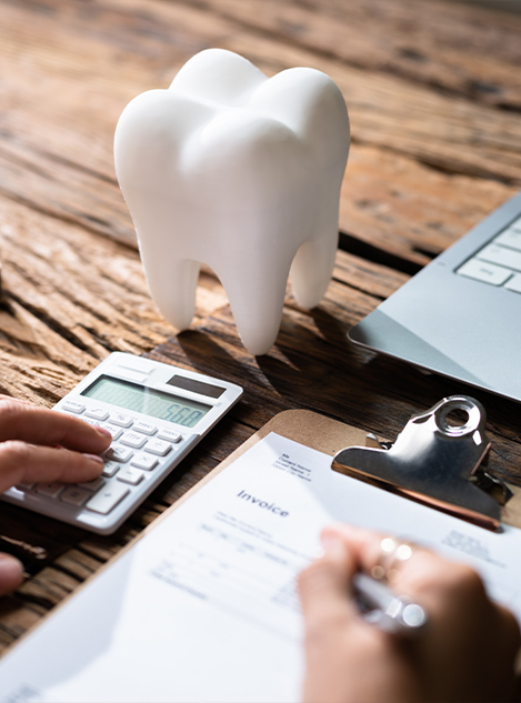 Person typing on calculator and writing on clipboard next to artificial tooth