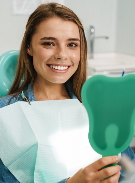 Young woman holding mirror and smiling in dental chair