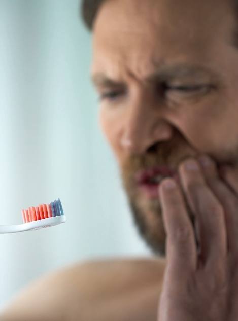 Man holding toothbrush with blood on it while touching his jaw in pain