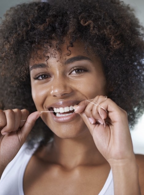 Woman in white tank top smiling while flossing her teeth