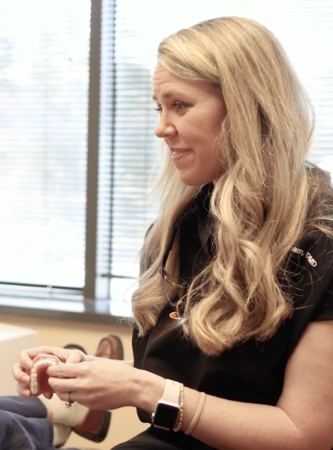 Doctor Grisham holding a denture while talking to a patient