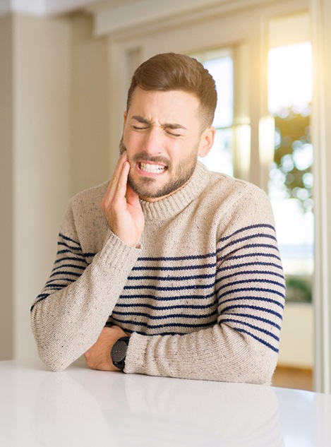 Man in striped sweater rubbing his jaw in pain