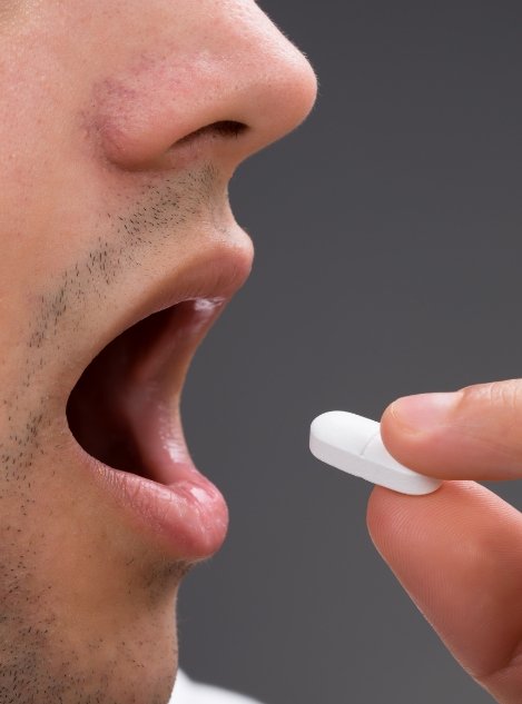 Man about to place a white pill in his mouth