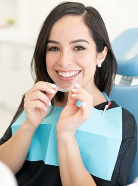 Happy dental patient holding SureSmile clear aligner