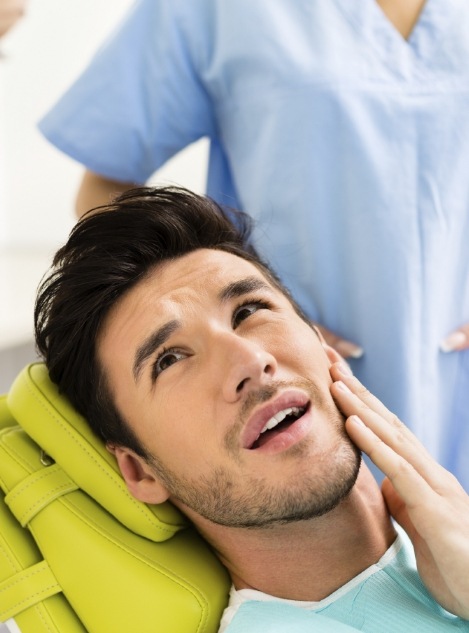 Man in dental chair holding the side of his face in discomfort