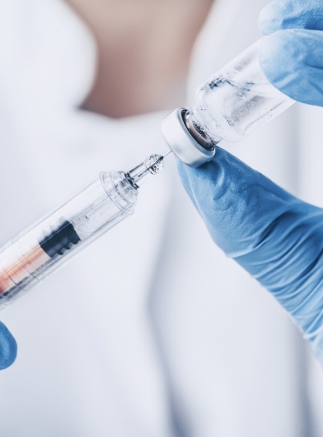 Person drawing clear liquid out of a vial and into a syringe