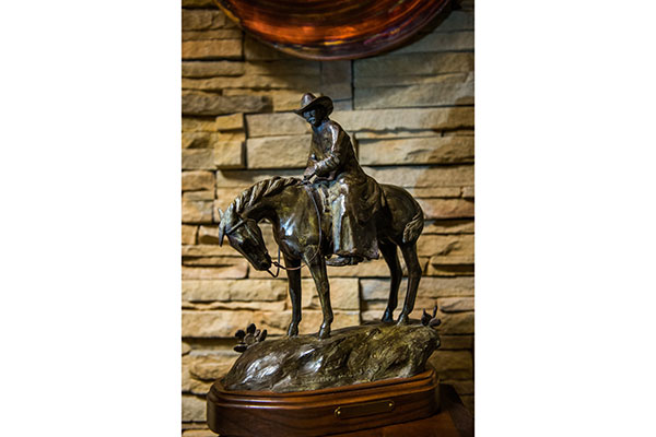 Black sculpture of man in cowboy hat riding horse