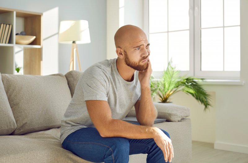 Man with tooth pain sitting on his couch