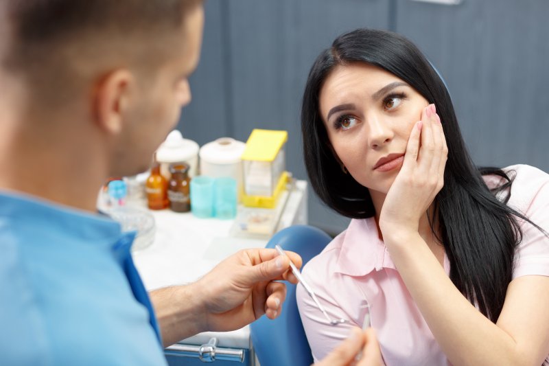 Woman holding her cheek in her hand looking up at dentist