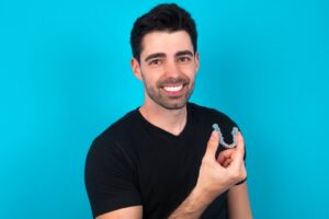 Man smiling while holding up his SureSmile clear aligner