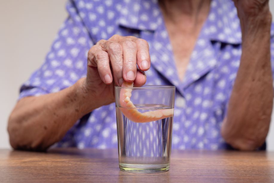 A woman putting her dentures in a glass of water.